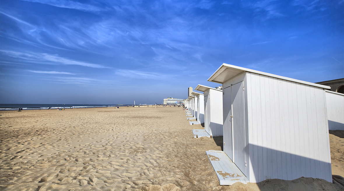 white beach huts on a long stretch of sandy beach under blue skies